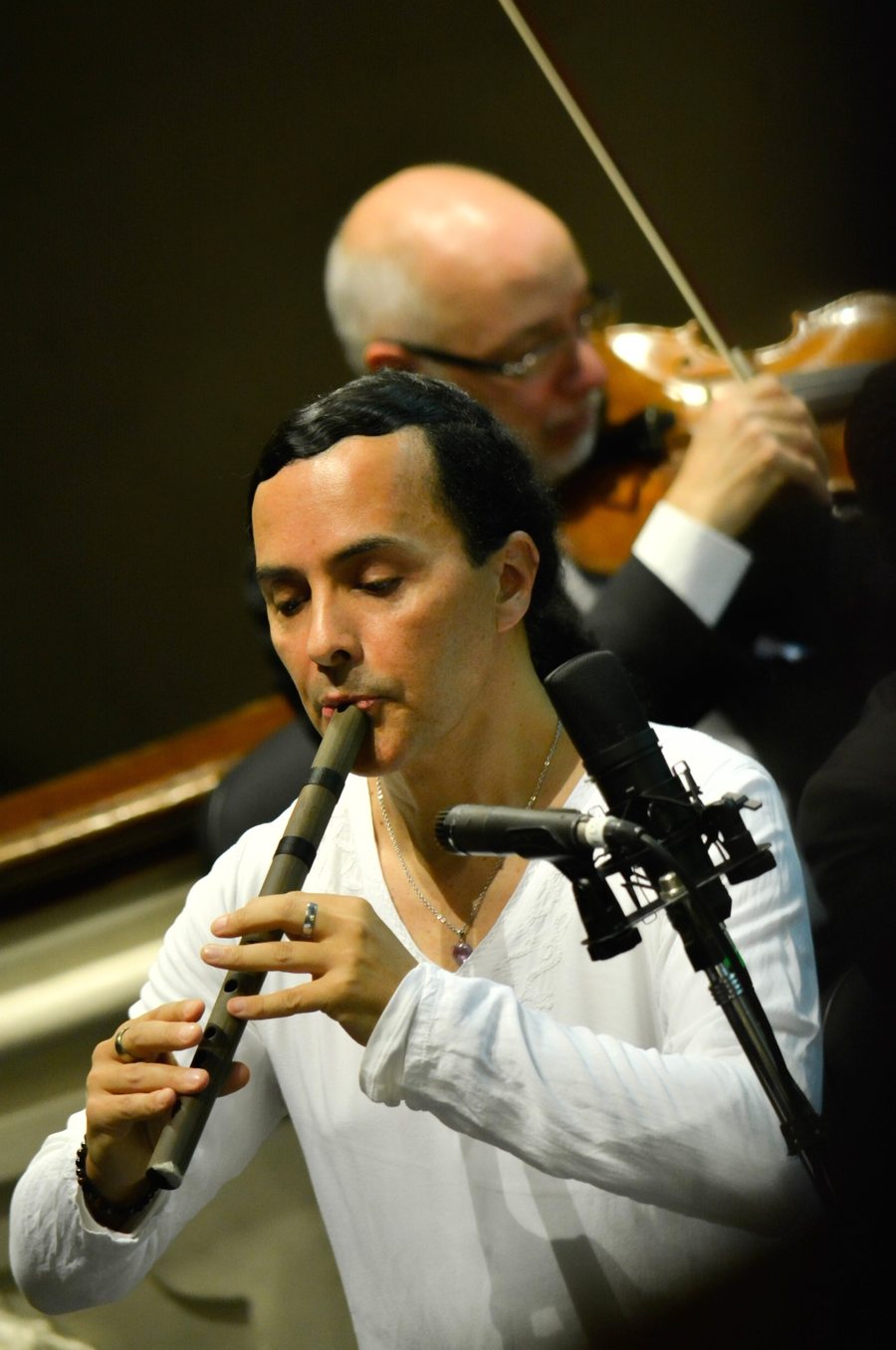 Pablo Salcedo performing the Markama chromatic quena on stage, beside the violins of the Mendoza Philharmonic Orchestra